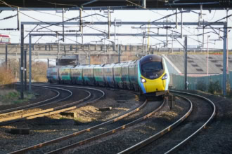 Avanti West Coast train travelling on curved tracks under overhead power lines in the UK.