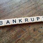 Scrabble tiles spelling the word “BANKRUPT” on a wooden table