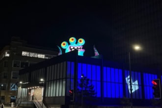 Colourful monster installation on a Manchester rooftop glowing at night during Halloween in the City.