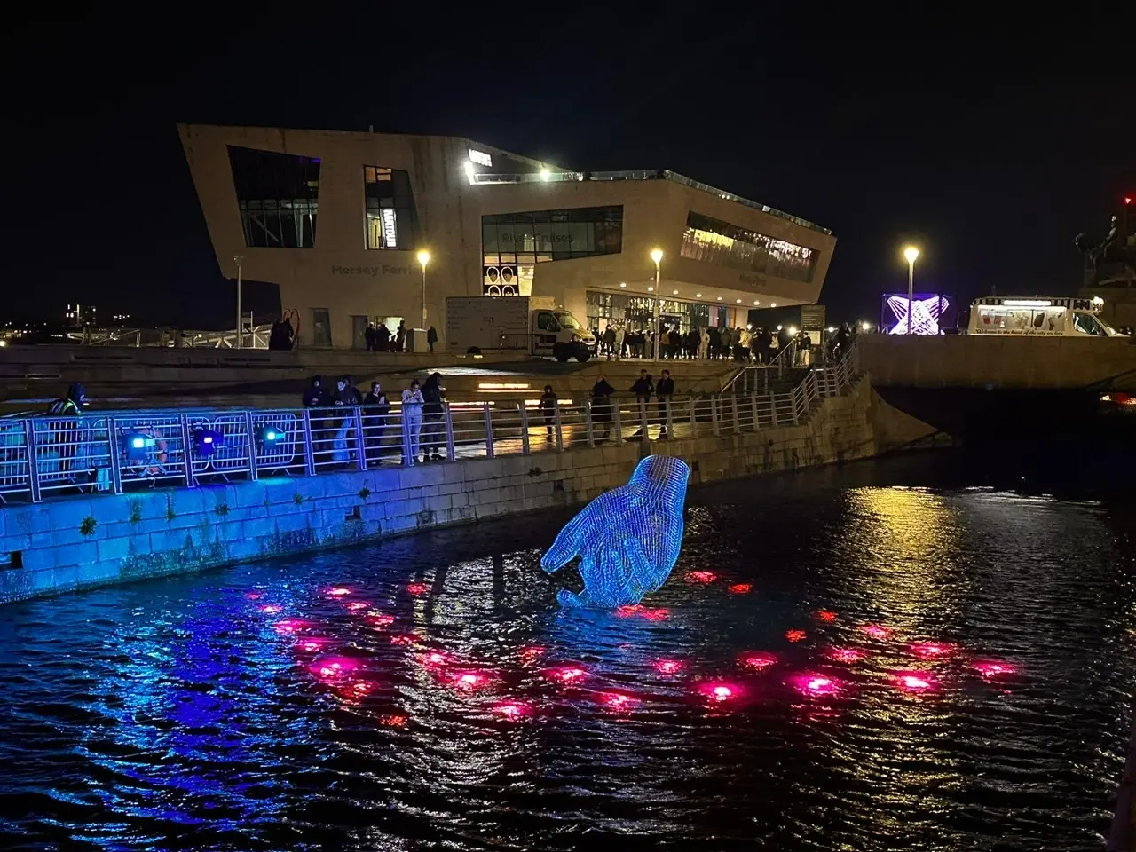 Blue illuminated hand sculpture floating in the River Mersey at Liverpool’s Pier Head during River of Light 2025 festival.