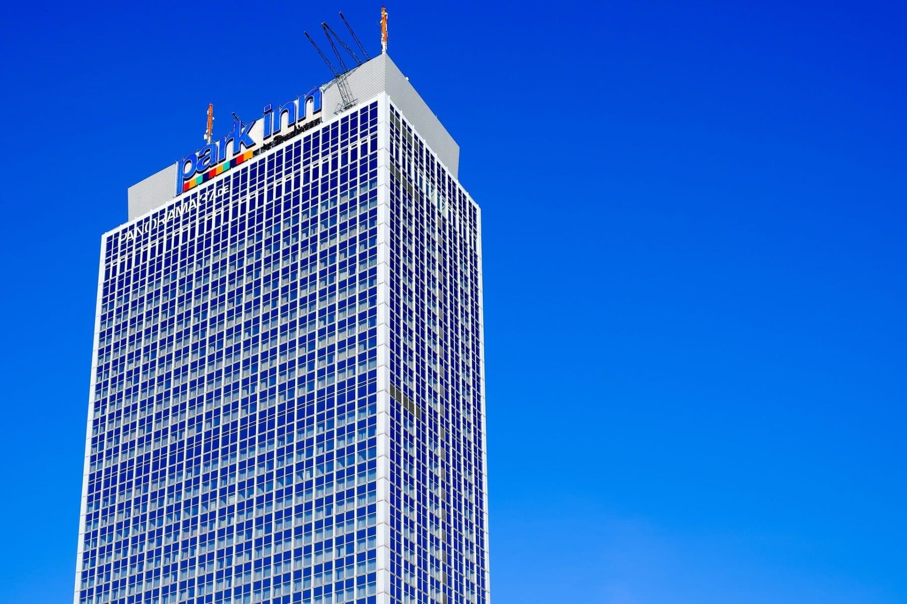 Exterior of a Park Inn hotel tower under a bright blue sky.