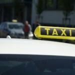 ellow taxi sign on top of a white car in a UK city street