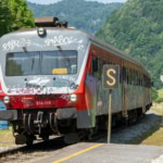 Slovenian regional train arriving at a rural station surrounded by green hills