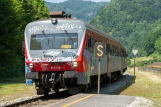 Slovenian regional train arriving at a rural station surrounded by green hills