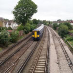 Southeastern train on suburban UK railway tracks surrounded by trees and houses