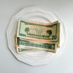 A stack of US dollar bills placed on a white patterned plate, symbolising tipping at restaurants.