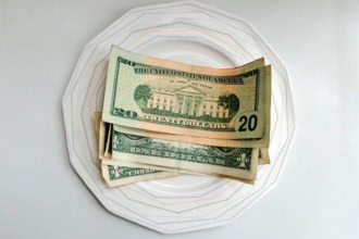 A stack of US dollar bills placed on a white patterned plate, symbolising tipping at restaurants.