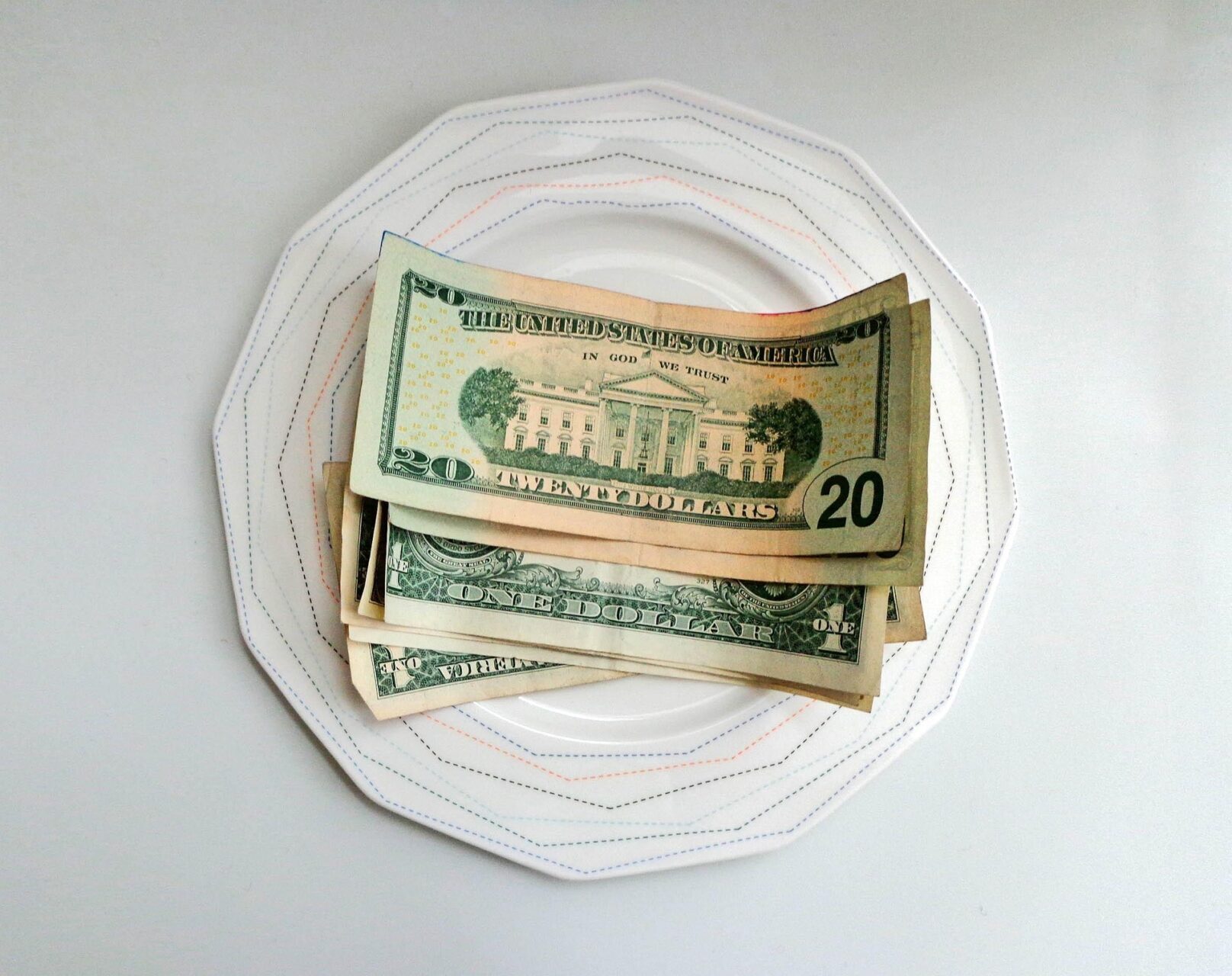 A stack of US dollar bills placed on a white patterned plate, symbolising tipping at restaurants.