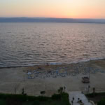 Sunset over the Dead Sea in Jordan with a quiet sandy beach and rows of empty sun loungers.