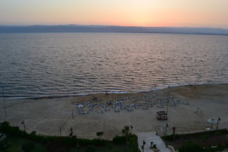 Sunset over the Dead Sea in Jordan with a quiet sandy beach and rows of empty sun loungers.