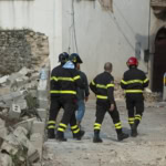 Rescue workers walking through earthquake debris and damaged buildings after a seismic event.