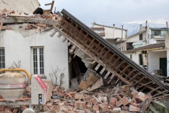 Collapsed residential building after an earthquake, with fallen roof beams, broken bricks and structural damage.
