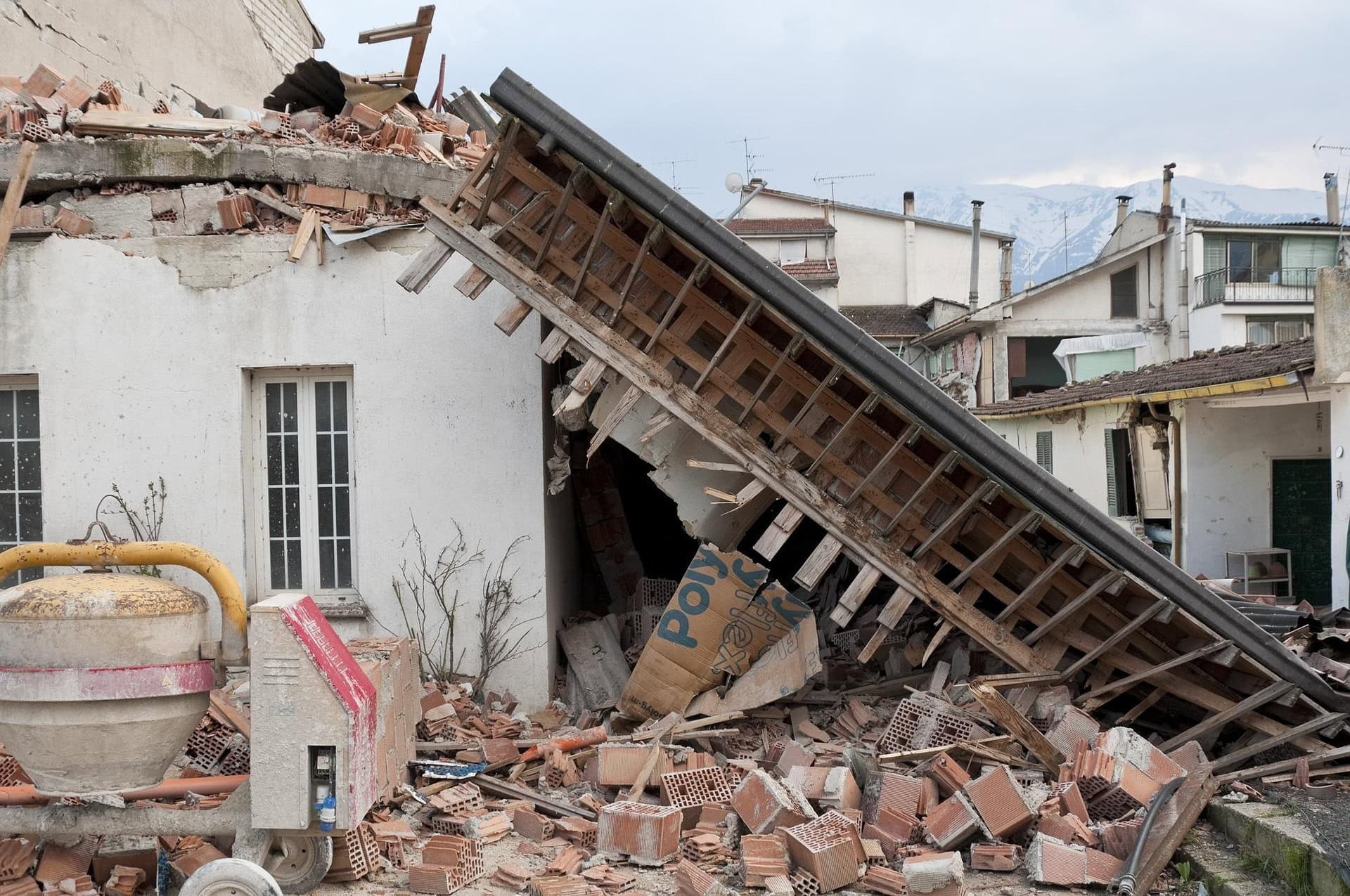 Collapsed residential building after an earthquake, with fallen roof beams, broken bricks and structural damage.
