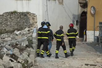 Rescue workers walking through earthquake debris and damaged buildings after a seismic event.