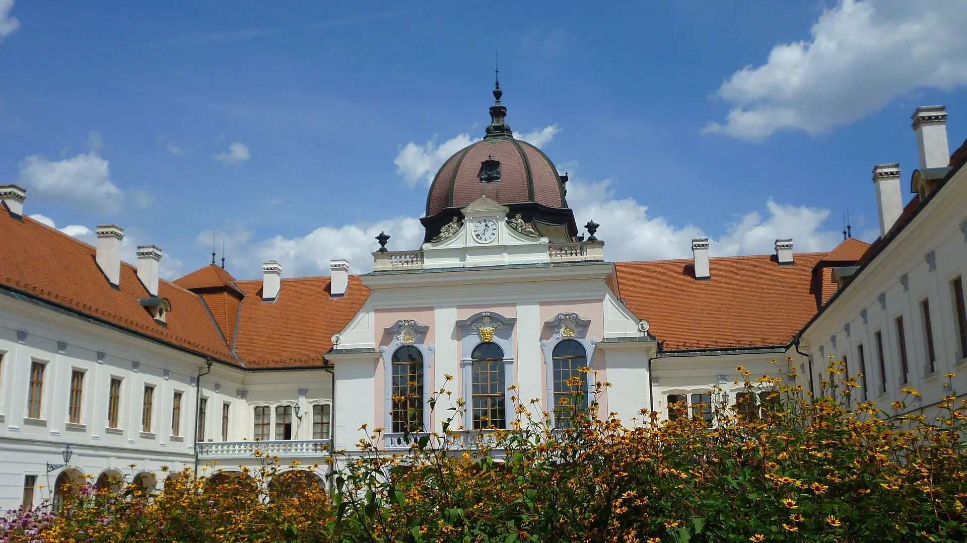 The main courtyard and dome of Gödöllő Royal Palace with flowers in the foreground.
