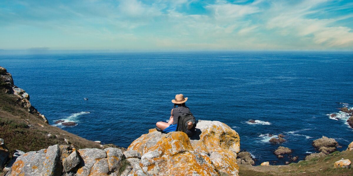 Traveller resting on a coastal cliff overlooking the sea, symbolising freedom and outdoor exploration — ideal for AllTrails hiking adventures.
