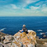 Traveller resting on a coastal cliff overlooking the sea, symbolising freedom and outdoor exploration — ideal for AllTrails hiking adventures.
