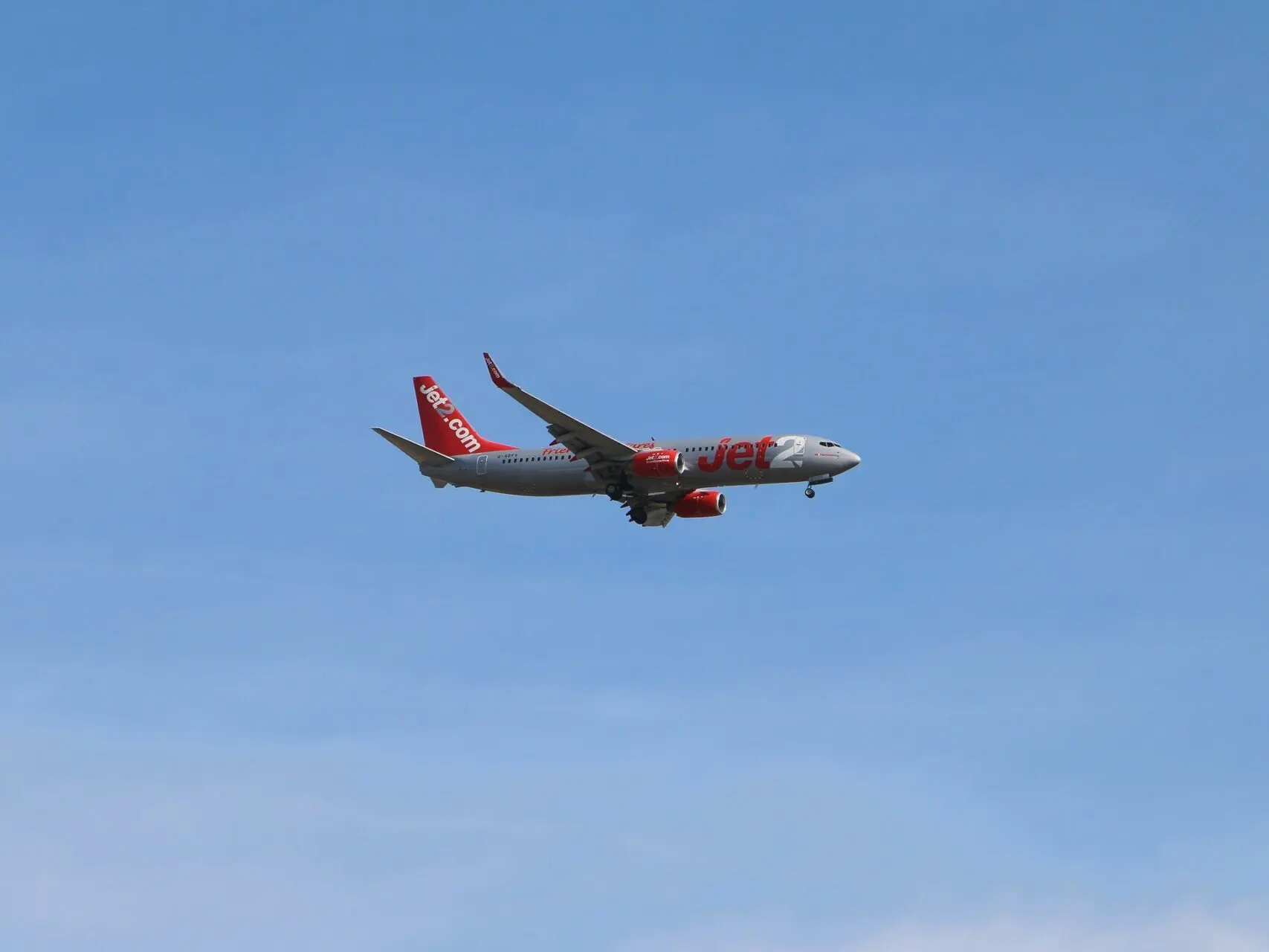 Jet2 aircraft flying in clear blue sky above clouds