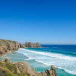 Turquoise waves and rocky cliffs at Porthcurno Beach near Penzance, Cornwall – a scenic coastal view reached by the Night Riviera Sleeper train from London.