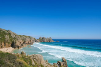 Turquoise waves and rocky cliffs at Porthcurno Beach near Penzance, Cornwall โ a scenic coastal view reached by the Night Riviera Sleeper train from London.