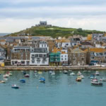St Ives harbour in Cornwall with colourful boats on the water and St Nicholas Chapel overlooking the town.