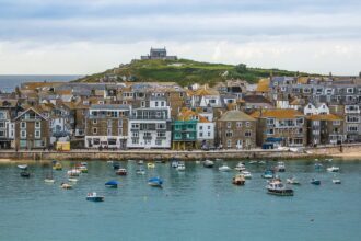 St Ives harbour in Cornwall with colourful boats on the water and St Nicholas Chapel overlooking the town.