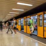 Passengers boarding a yellow Budapest metro train at an underground station platform