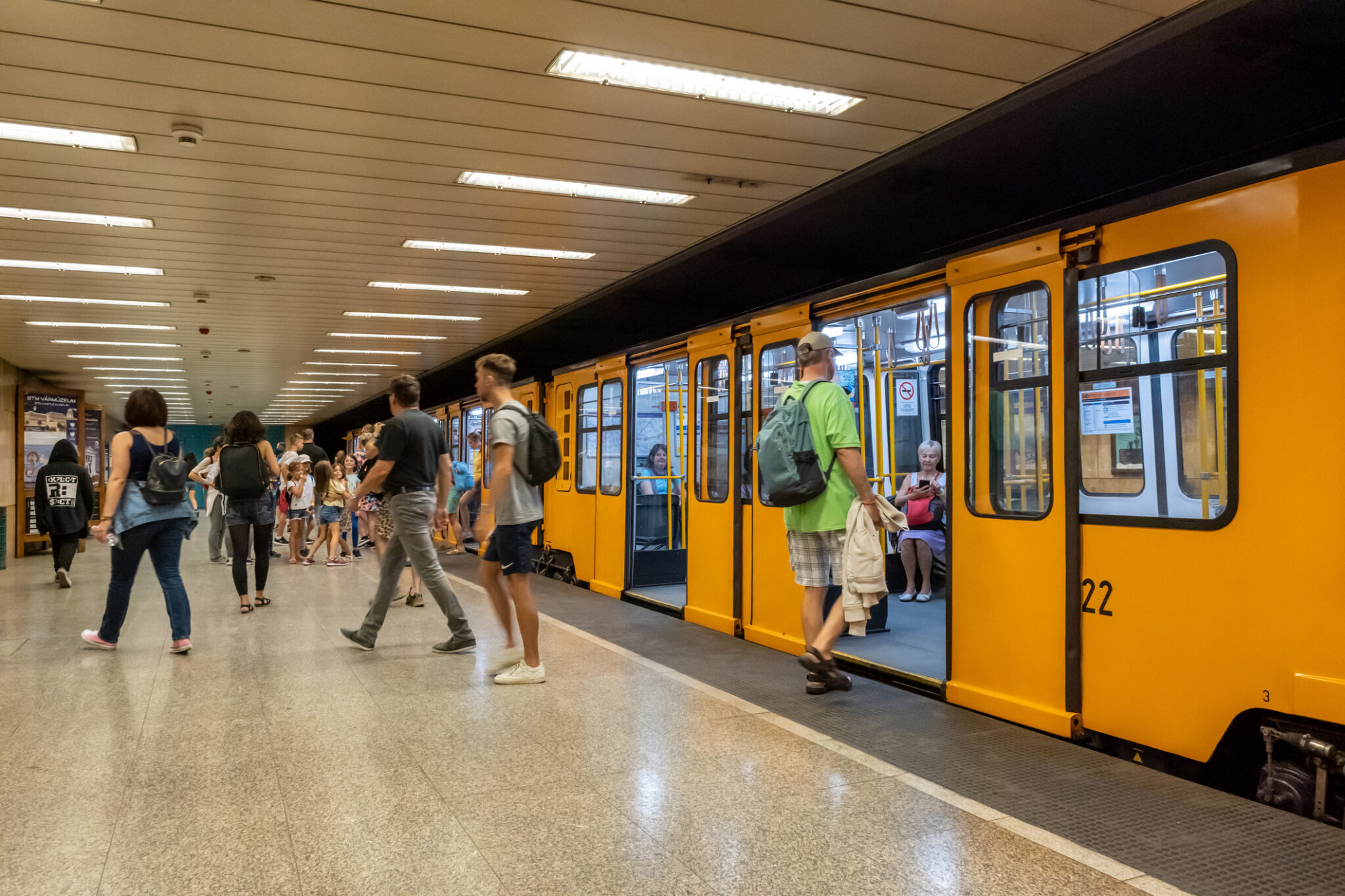 Passengers boarding a yellow Budapest metro train at an underground station platform