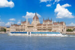 Hungarian Parliament Building in Budapest seen from the Danube with a river cruise boat passing in front