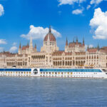 Hungarian Parliament Building in Budapest seen from the Danube with a river cruise boat passing in front