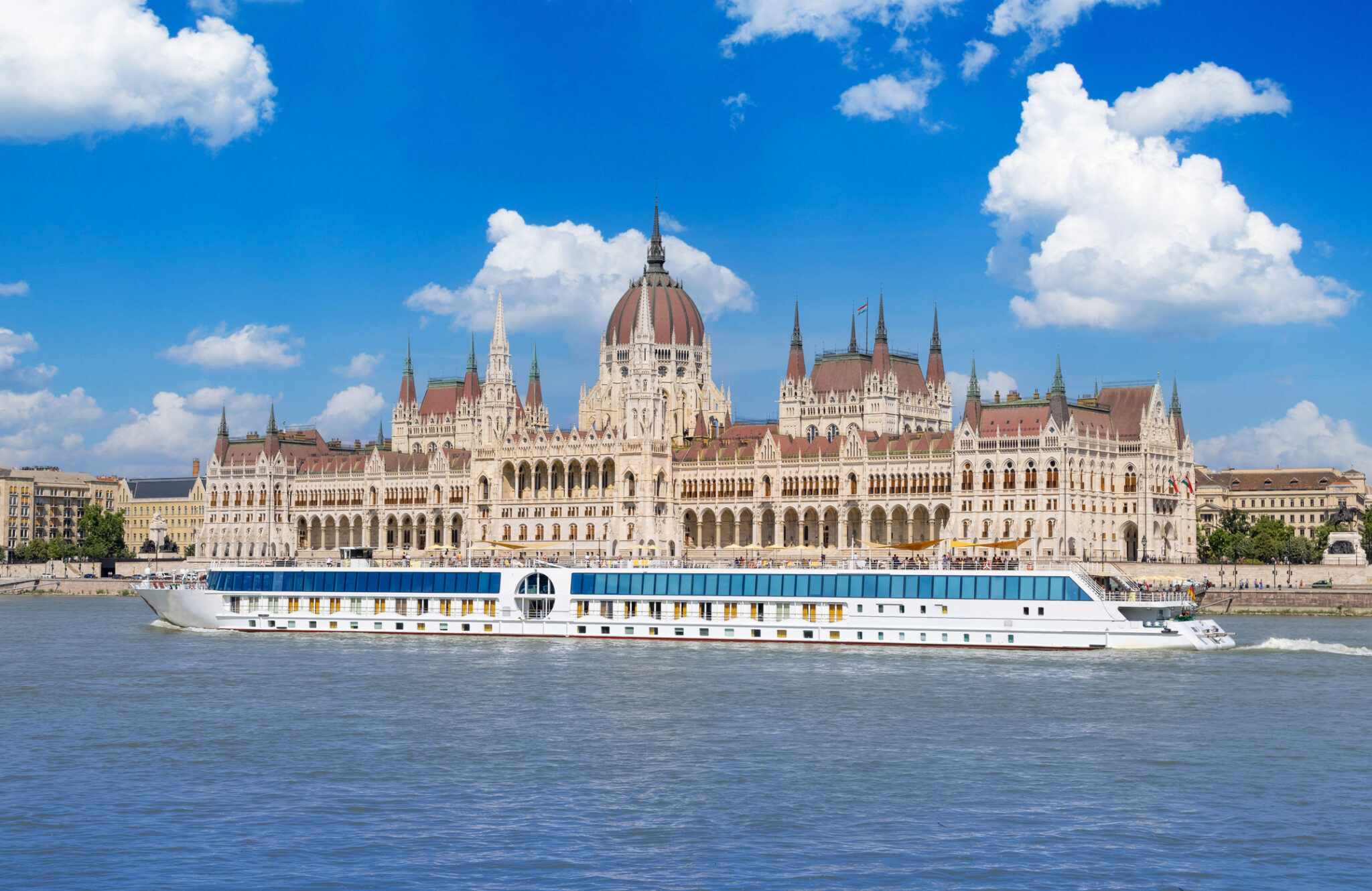 Hungarian Parliament Building in Budapest seen from the Danube with a river cruise boat passing in front