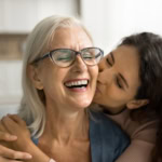 Daughter kissing her smiling mother on the cheek while celebrating Mother’s Day