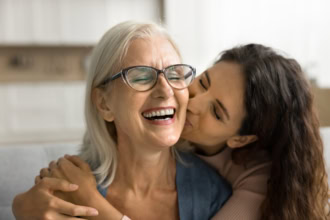 Daughter kissing her smiling mother on the cheek while celebrating Motherโs Day