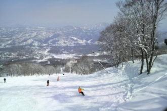 Skiing in Japan with wide groomed slope and mountain views in the background