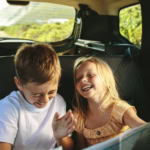 Two children laughing in the back seat of a car during a family road trip