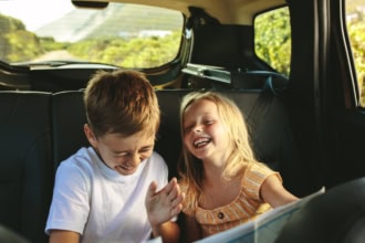 Two children laughing in the back seat of a car during a family road trip