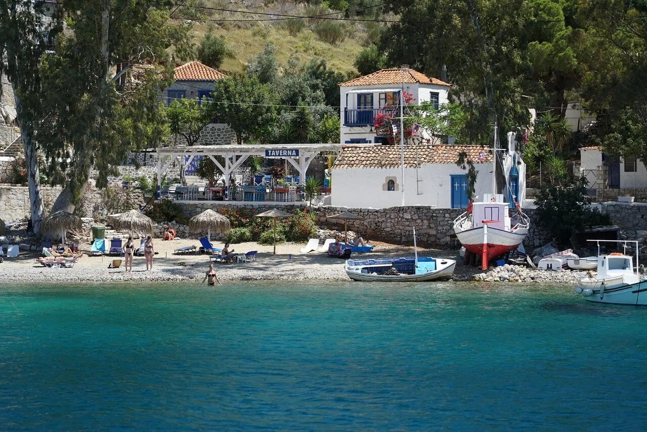 Hydra island beach with taverna and traditional coastal village Greece