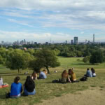 View of London skyline from Primrose Hill with people sitting on the grass