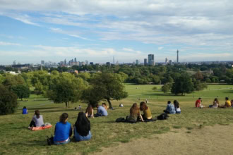 View of London skyline from Primrose Hill with people sitting on the grass