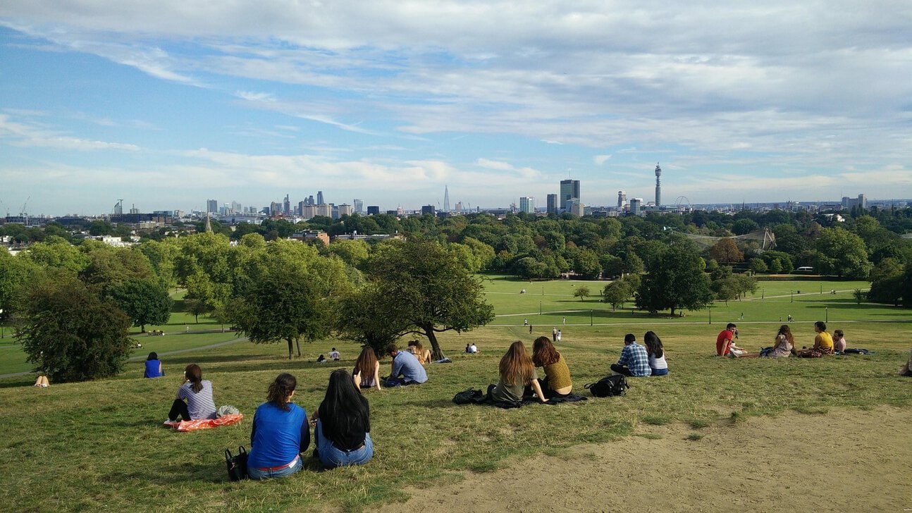 View of London skyline from Primrose Hill with people sitting on the grass
