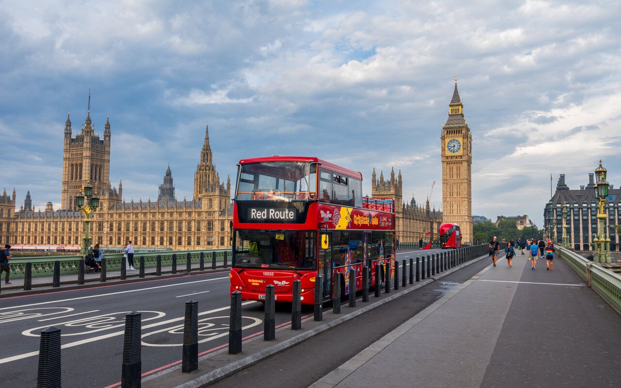 Hop on hop off bus crossing Westminster Bridge with Big Ben and Houses of Parliament in London