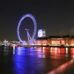 London Eye illuminated at night reflected in the River Thames