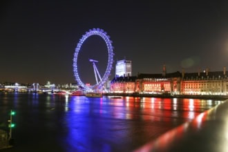 London Eye illuminated at night reflected in the River Thames