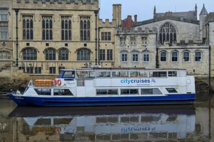 City Cruises boat on the River Ouse in York with historic buildings behind