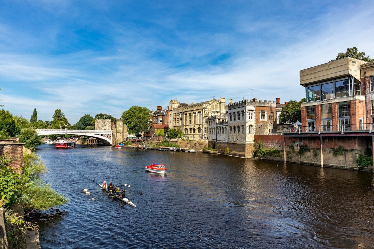Boats and rowers on the River Ouse in York near a bridge and historic buildings