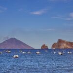Small boats floating on the sea near the volcanic islands of Stromboli and Lipari in the Aeolian Islands, Sicily, during a calm Mediterranean evening.