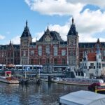 Amsterdam Centraal Station with canal boats and tram in front of the main entrance