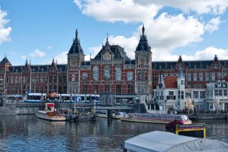 Amsterdam Centraal Station with canal boats and tram in front of the main entrance