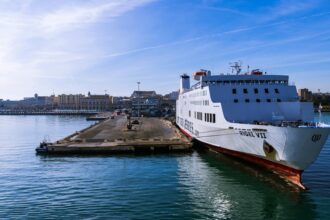 Large passenger ferry docked at Bari Port in Puglia, Italy, with the Adriatic Sea and Bari waterfront in the background.