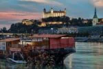 Bratislava Castle illuminated above the Danube River at sunset with boats along the Bratislava waterfront in Slovakia